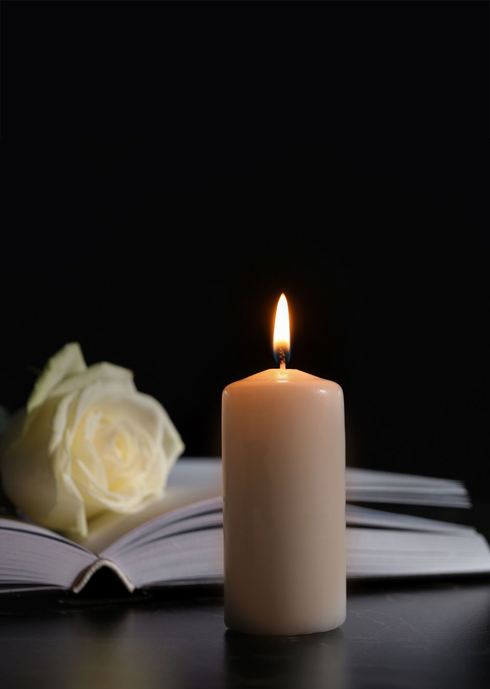 Brennende Kerze mit einem Buch und weißer Rose im Hintergrund